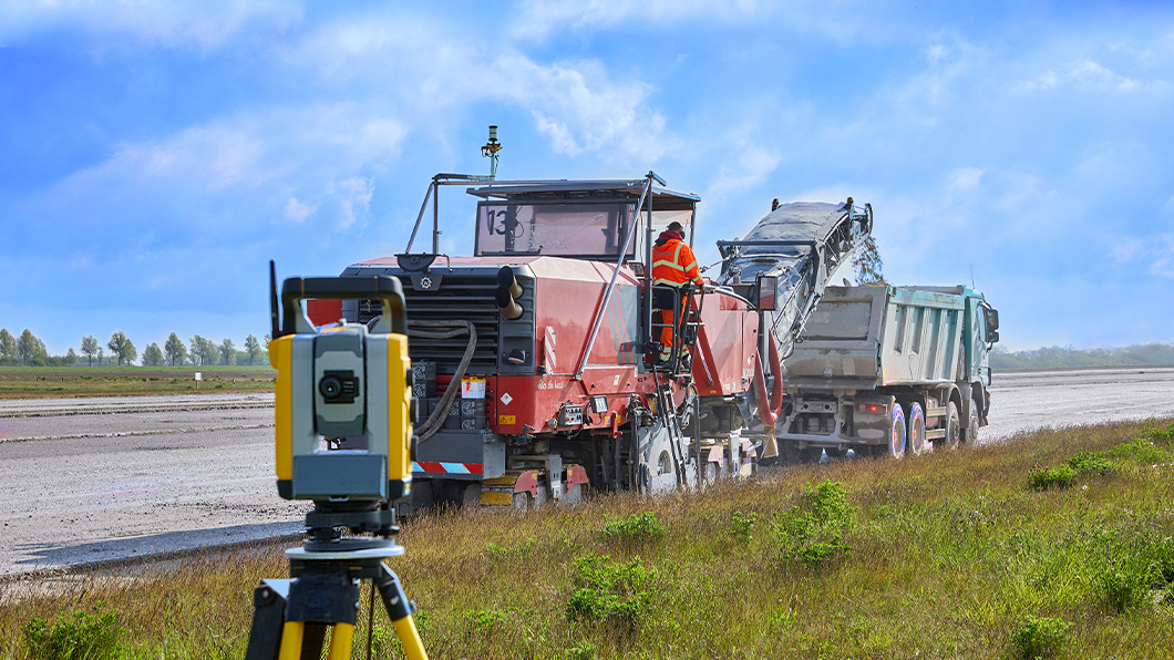 Trimble SPS Total Station surveying with Trimble Roadworks operating on a milling machine loading material into a dump truck in the background